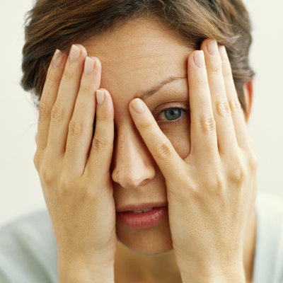Young woman covering face with hands, looking through fingers, close-up